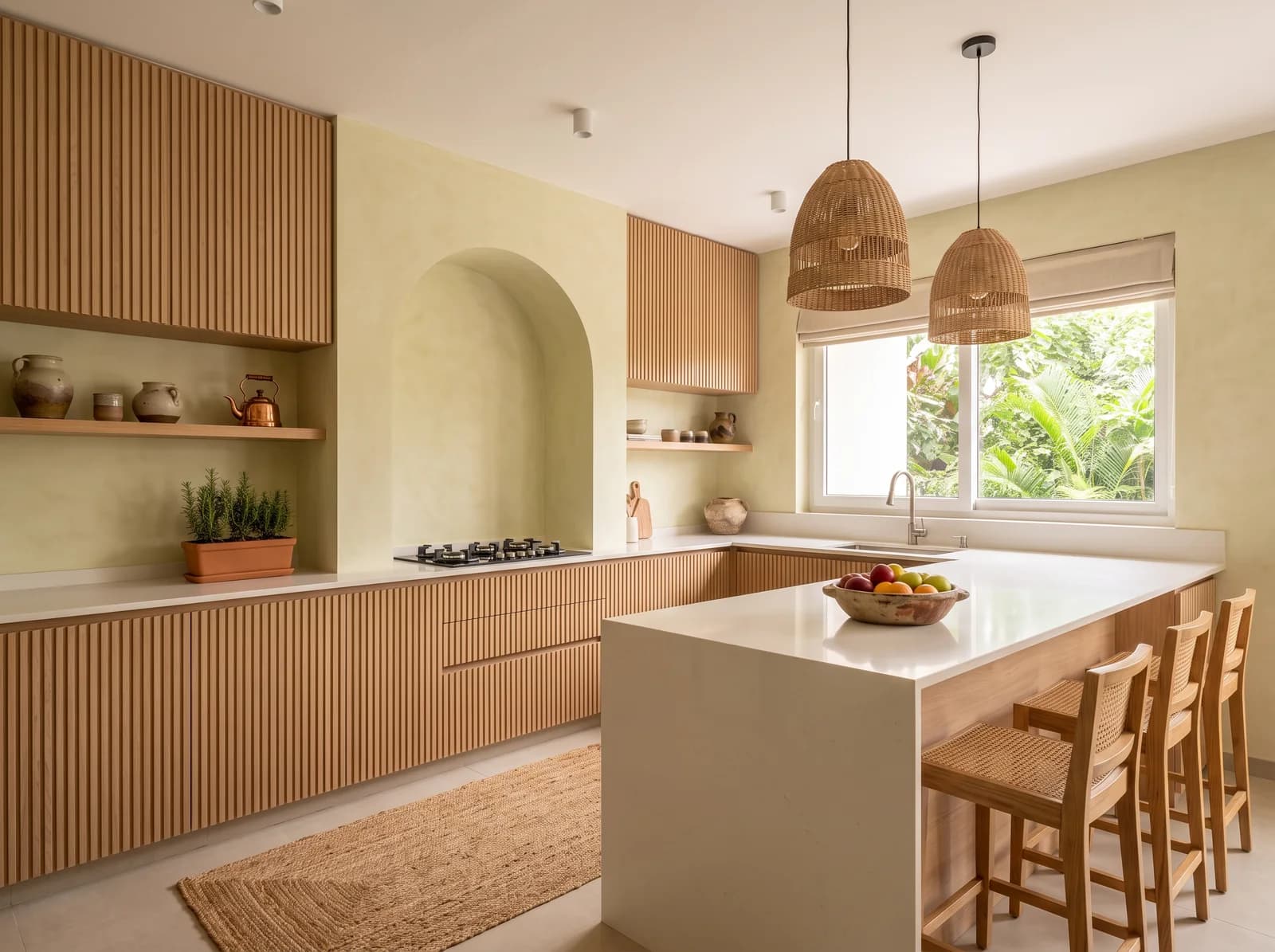Japandi kitchen with slatted oak cabinets, a plain plaster arch over the hob, a white quartz island with rattan stools and woven pendants